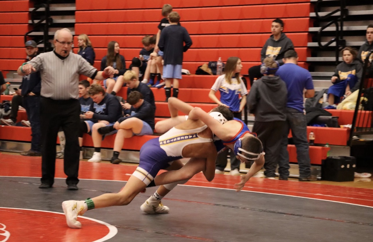 Black and white photograph of a live wrestling takedown on the mat